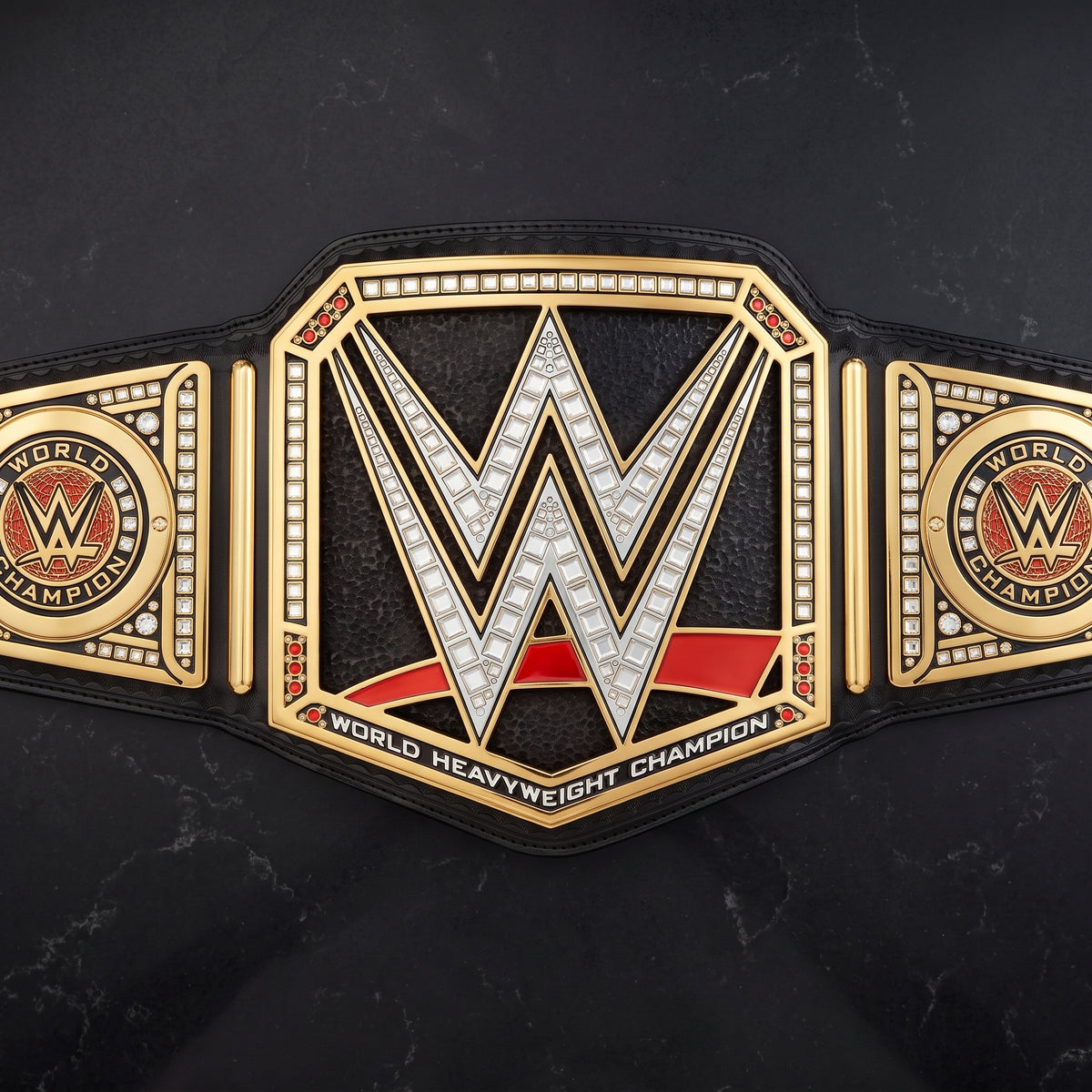 A WWE World Heavyweight Championship belt displayed flat against a dark marble background. The belt features a large central gold-toned plate with a silver WWE 'W' logo outlined in black, flanked by two side plates with WWE emblems and the words 'World Champion'.