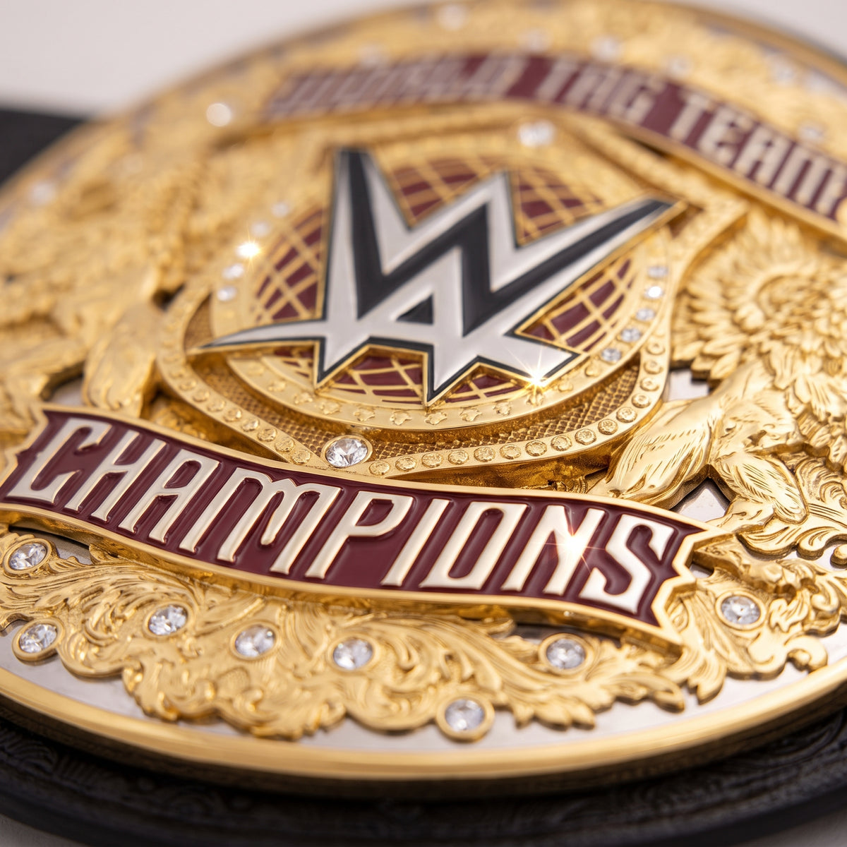Close-up of a gold WWE Championship belt with maroon and silver details, featuring the WWE logo and the words 'CHAMPIONS' and 'BUILD A TEAM'.