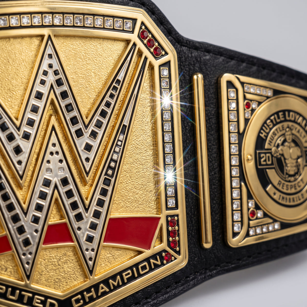Close-up of a gold and black wrestling championship belt with a large WWE-style W logo and a round 'Hustle Loyalty 2025 Respect' medallion, shown on a light gray background.