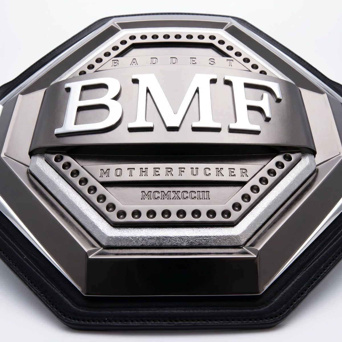 A close-up of a metallic octagonal belt with a black leather strap, featuring raised silver lettering that reads 'SMUTDEST BMF' and 'MOTHERFUCKER' with the Roman numeral 'MCMXCVIII'.