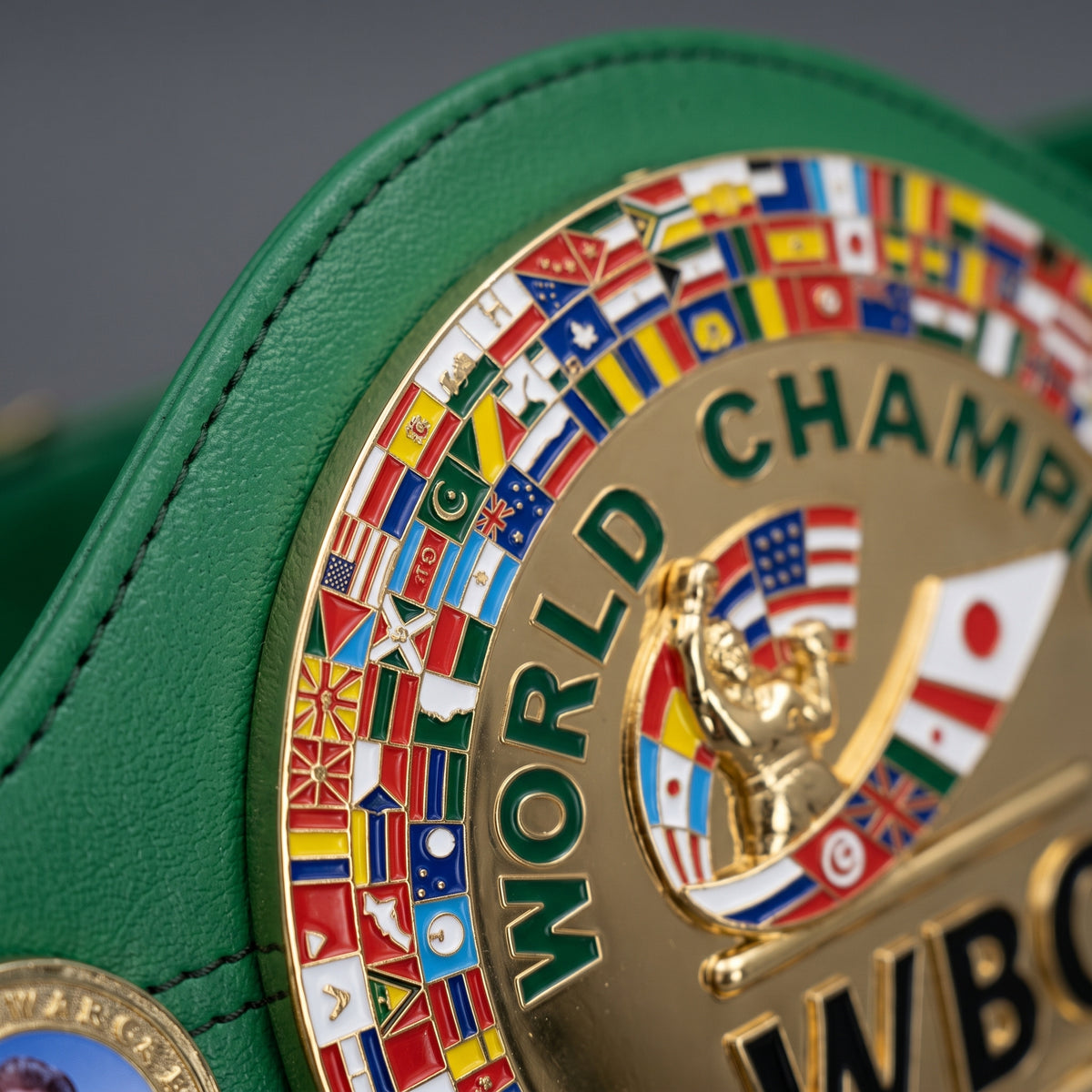 Close-up of a green leather belt with a large gold-toned metal medallion featuring the words "WORLD CHAMP" and surrounded by many colorful national flags.