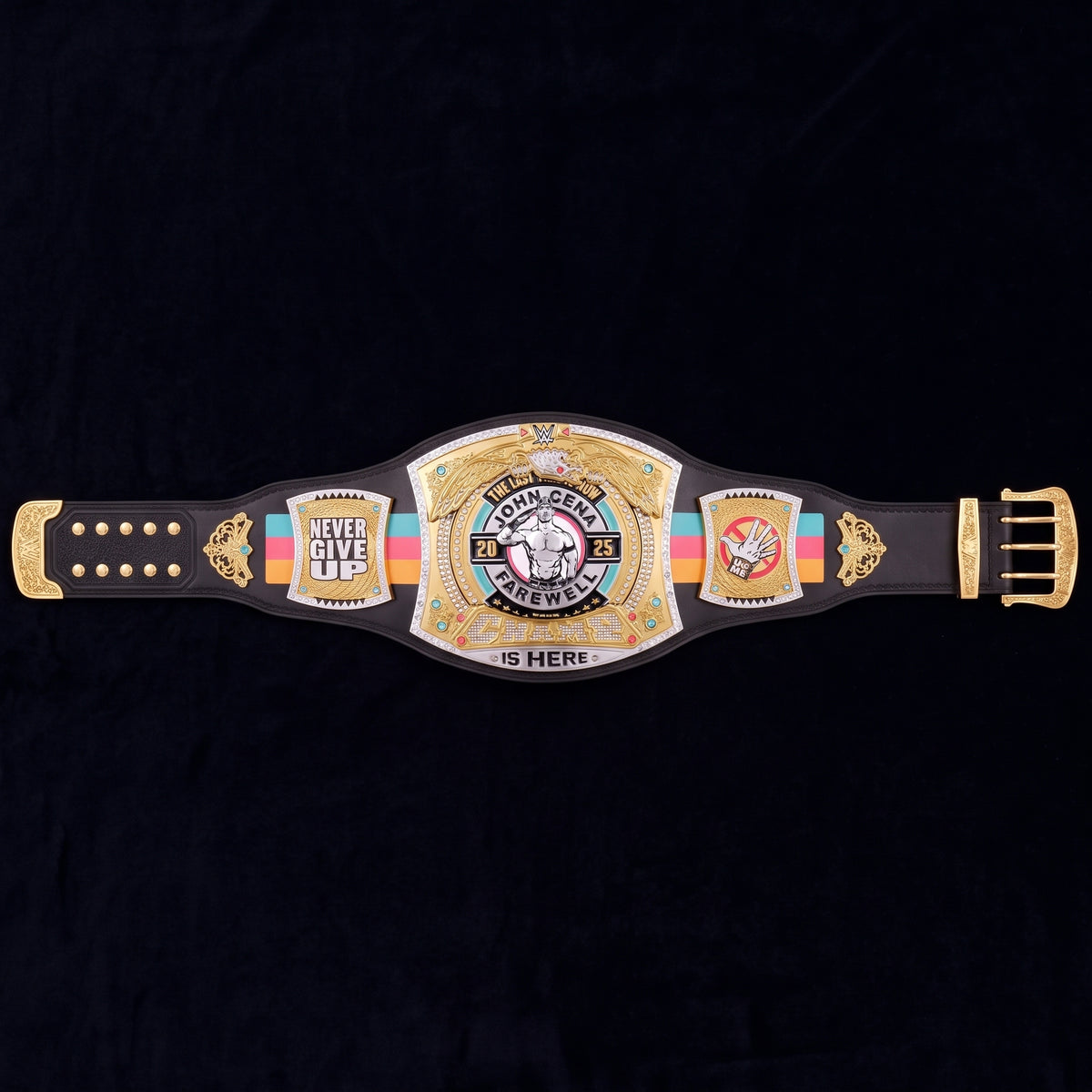 A custom championship belt featuring a black leather strap with gold-plated hardware and a large central plate. The plate is decorated with gold, silver, and multicolor accents, including a rainbow stripe and a central circular emblem with a skull and crossbones.
