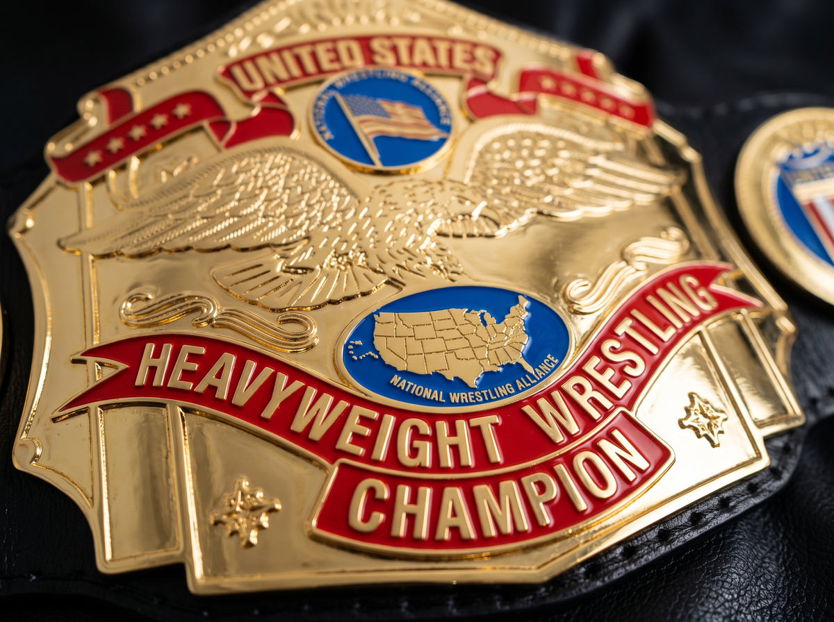 A close-up of a gold and red United States Heavyweight Wrestling Champion belt buckle with an eagle design and blue National Wrestling Alliance logo, resting on black leather.