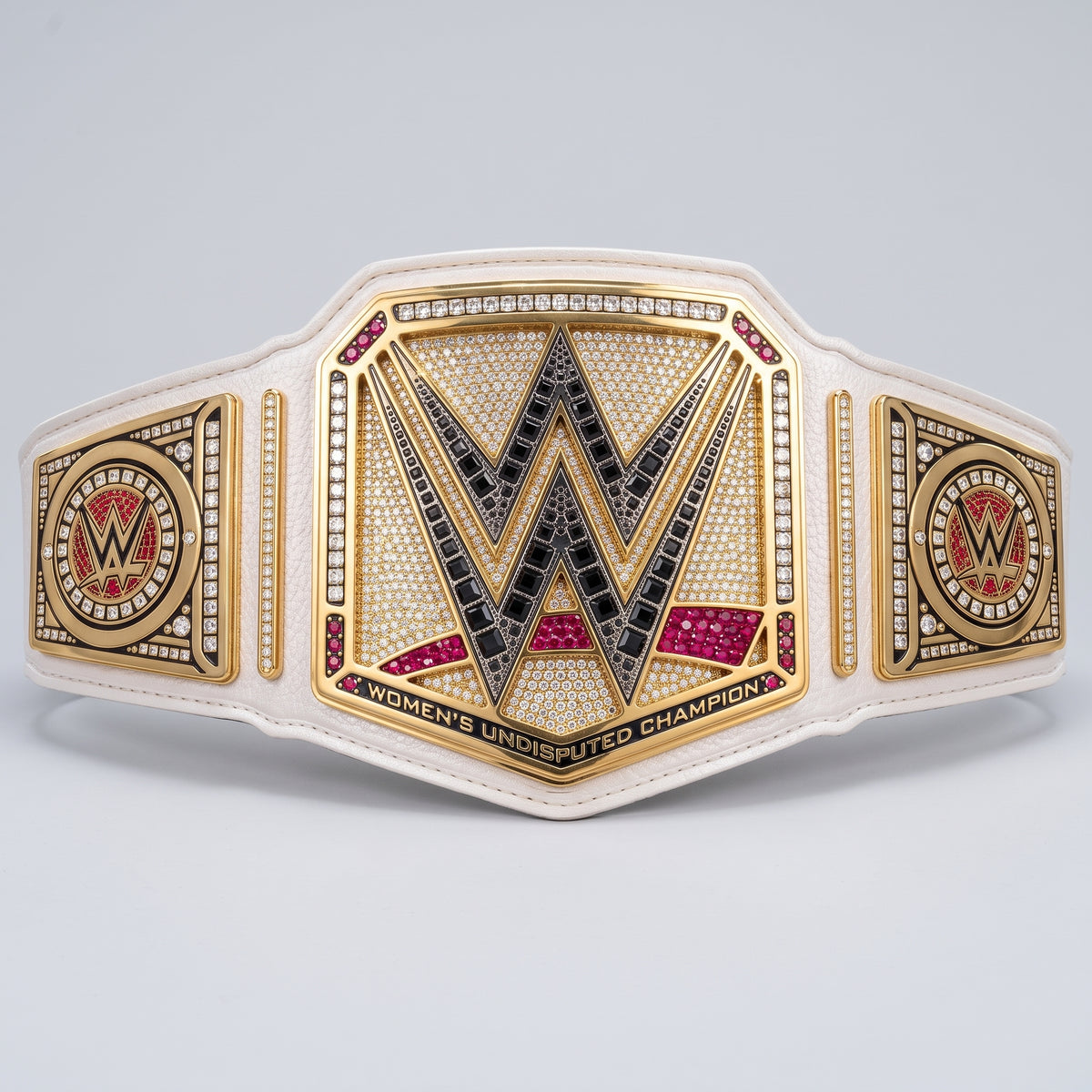WWE Women's Undisputed Champion belt featuring a large central 'W' emblem with black and gold detailing, flanked by two side medallions, on a white leather strap with rhinestone accents, photographed on a light gray background.