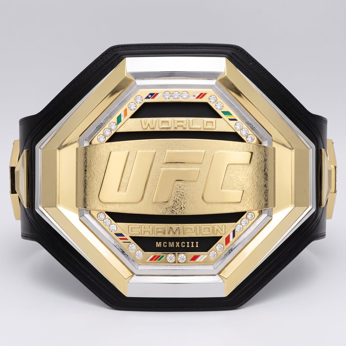A gold and silver UFC World Champion octagonal belt with a black strap, featuring a central gold plaque with the embossed UFC logo, crystal accents, and 'CHAMPION' and 'MCMXCIII' text.