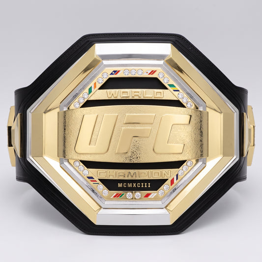 A gold and silver UFC World Champion octagonal belt with a black strap, featuring a central gold plaque with the embossed UFC logo, crystal accents, and 'CHAMPION' and 'MCMXCIII' text.
