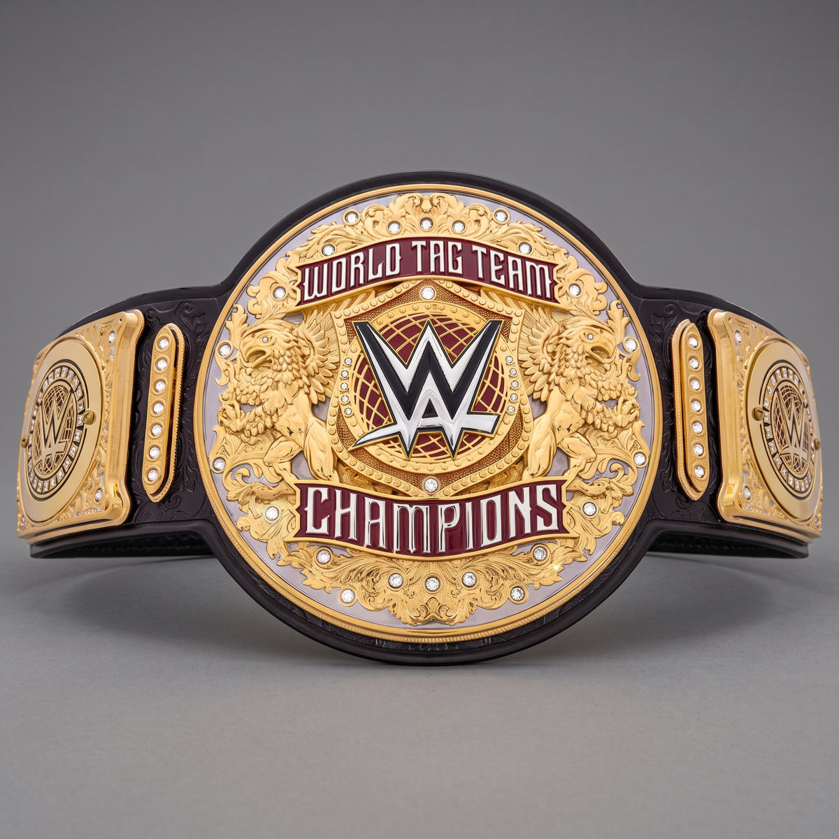 A WWE World Tag Team Champions belt with a large central gold-toned plate featuring the WWE logo, flanked by two side plates and a black strap, photographed on a neutral gray background.