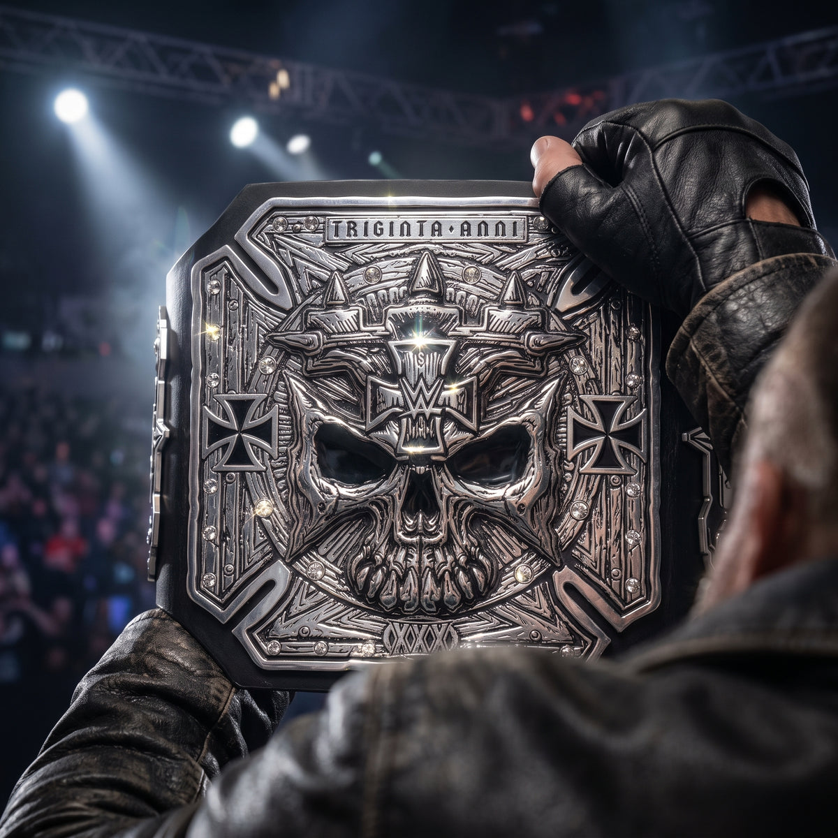 A close-up of a person in a black leather jacket and glove holding a large, ornate metallic championship belt featuring a skull design and the text 'TRICONTA ANNI' at the top. The background shows a blurred arena crowd and stage lights.