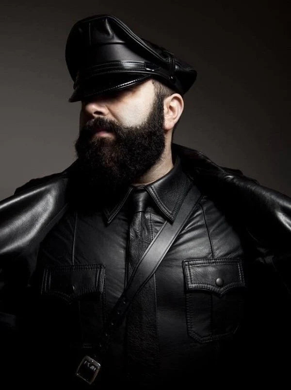 Man wearing a black leather outfit with a cap against a dark background